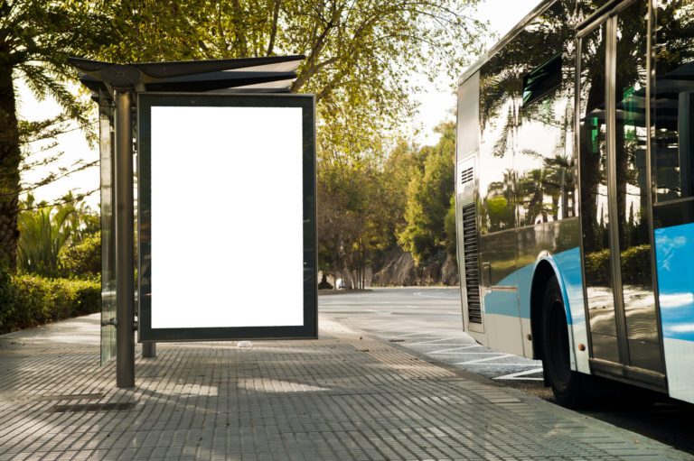 White blank vertical billboard at the bus stop on the city street. In the background of buses and roads. Sketch. Poster on the street next to the road