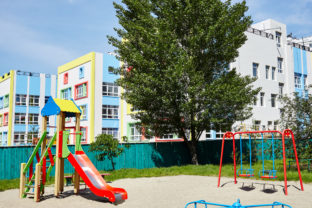 Facade of kindergarten building. Colorful playground for childrens on a sunny day with a blue sky
