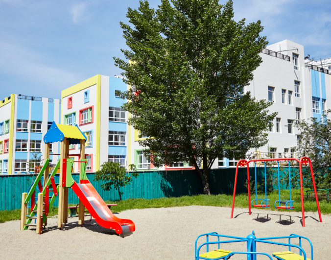 Facade of kindergarten building. Colorful playground for childrens on a sunny day with a blue sky