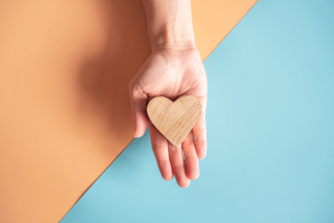 Hands holding wood heart on blue and orange color paper background, health care.