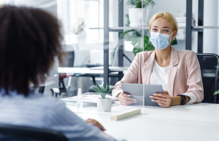 New normal and modern interview during covid 19 outbreak. HR manager with laptop looks at african american woman through protective glass