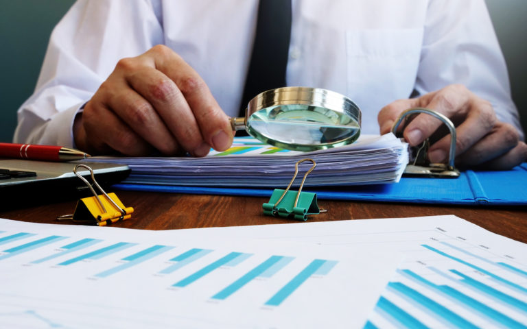 Auditor makes internal audit of company and checks financial report with magnifying glass.