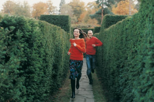 Front View Portrait of a Smiling Young Woman Running in a Maze Chased By a Young Man