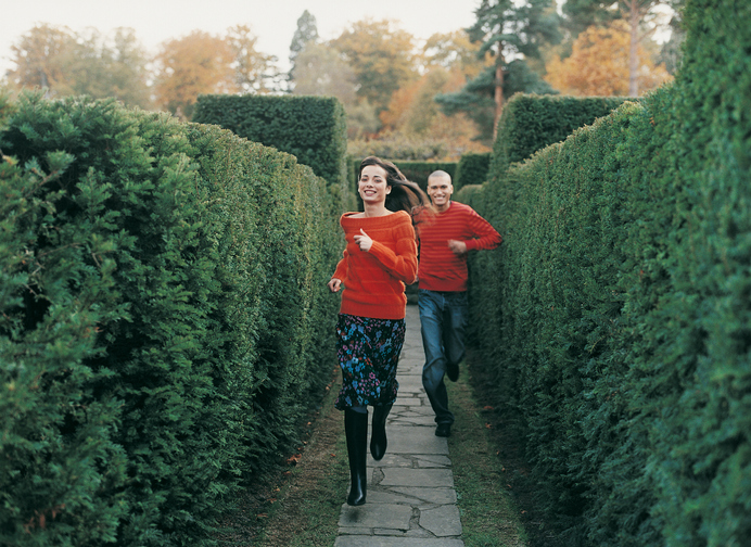 Front View Portrait of a Smiling Young Woman Running in a Maze Chased By a Young Man