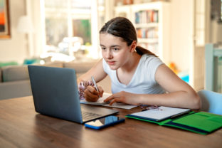 Teenager girl studying online at home looking at laptop at  quarantine isolation period during pandemic. Home schooling. Social distancing. Online school test.