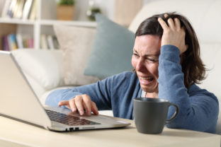 Sad adult woman crying reading bad news on laptop at home