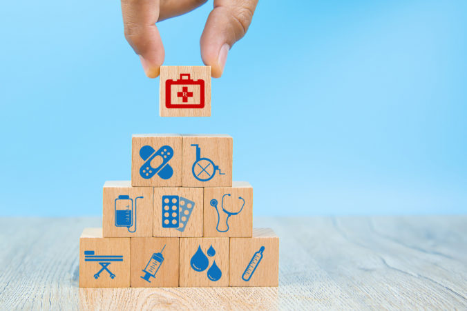 Close up hand choose Health care and medical symbols on wooden blocks toy stacked in Pyramid shape for health insurance concepts.