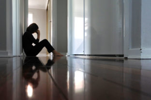 Sad woman sitting on dark home corridor floor.