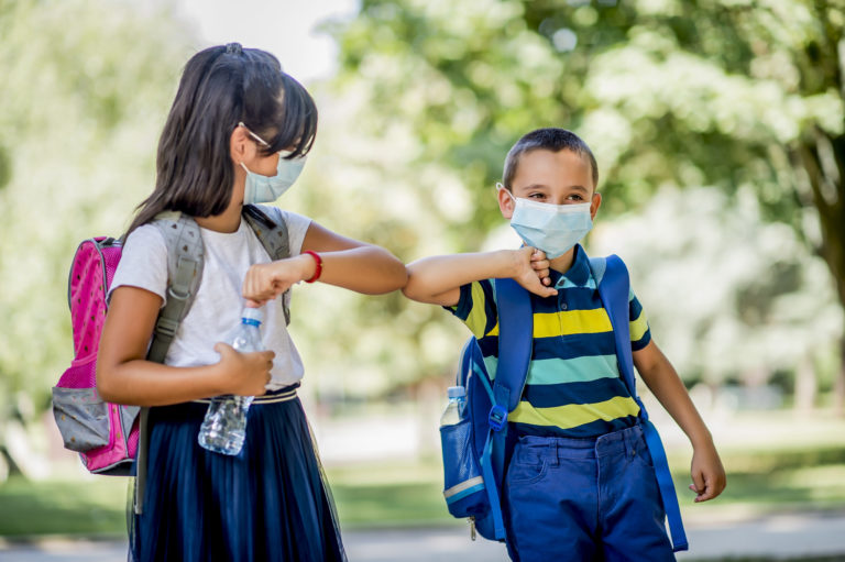 Two school children using elbow bump as an alternative handshake outdoors