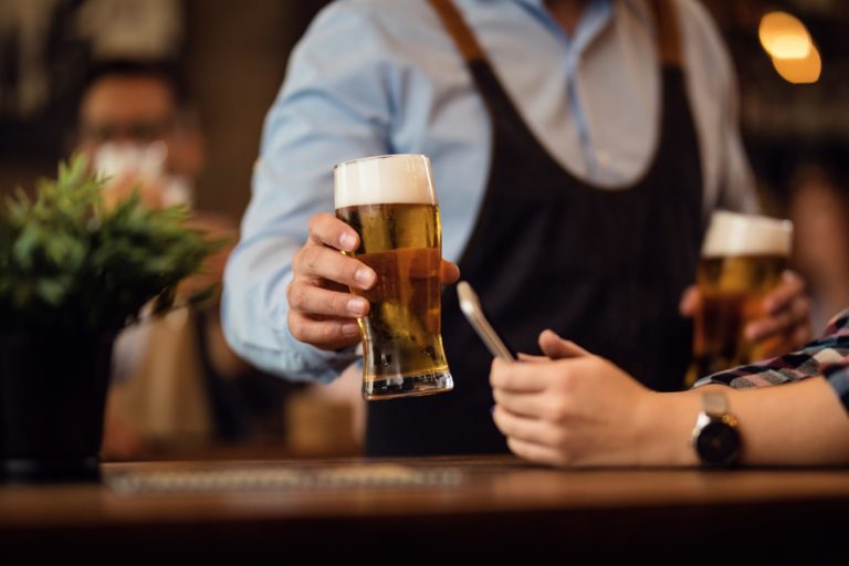 Close up of waiter serving a beer to his customer in a bar.
