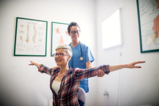 Beautiful cheerful professional nurse doing some physiotherapy exercises with patient.