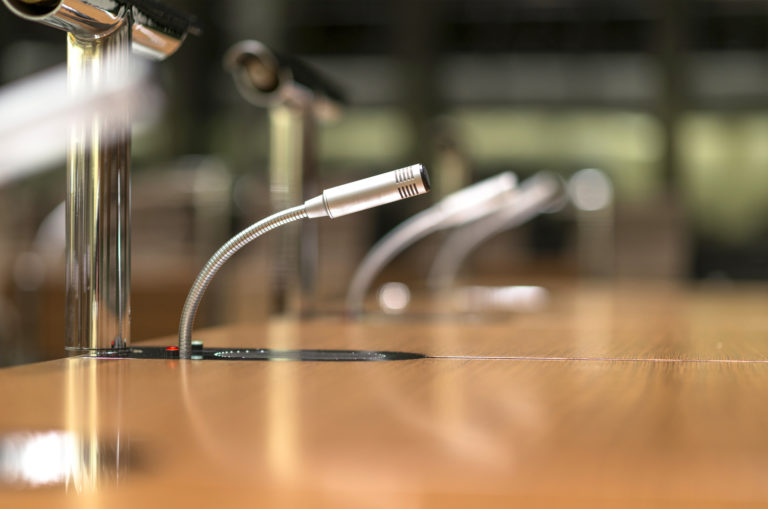 Isolated view of a microphone in the front of a conference room among blurred other mikes in the background