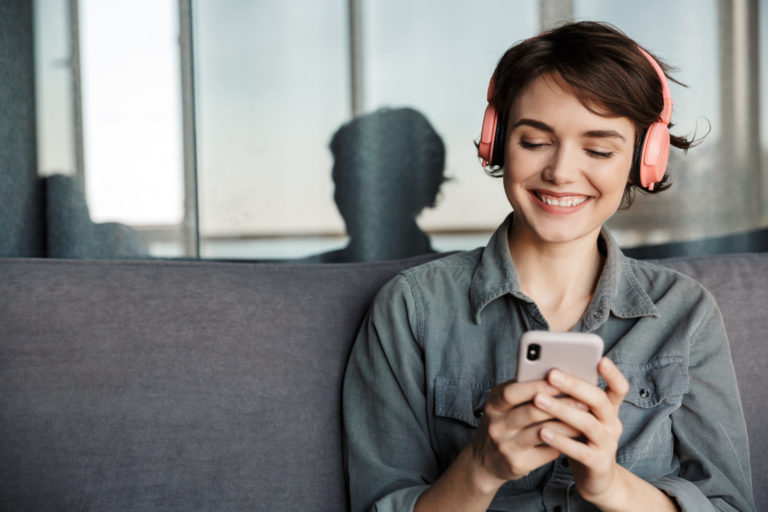 Image of nice young smiling woman using smartphone and headphones