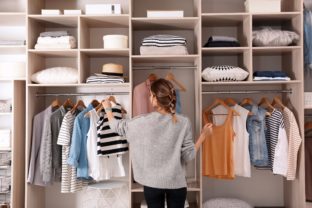 Woman choosing outfit from large wardrobe closet with stylish cl