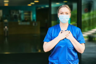 Young female scrub nurse wear blue uniform and face mask, standing in hospital entrance