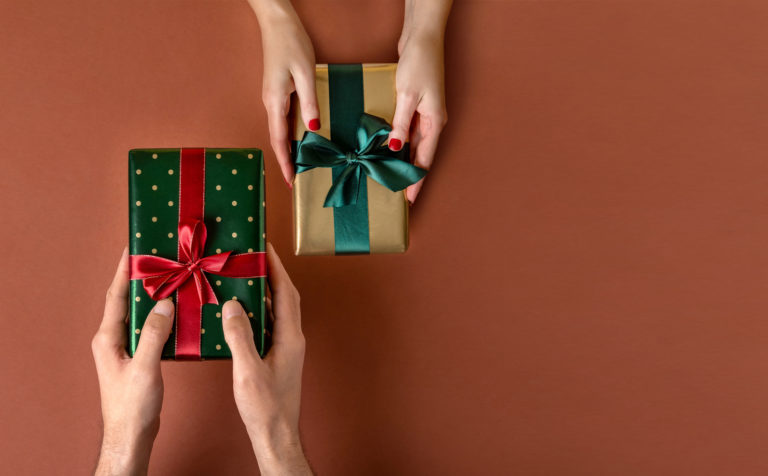 Woman giving her boyfriend a wrapped Christmas gift.Christmas giftboxes with tidewater green ribbon. Hands Giving Gifts Close up.