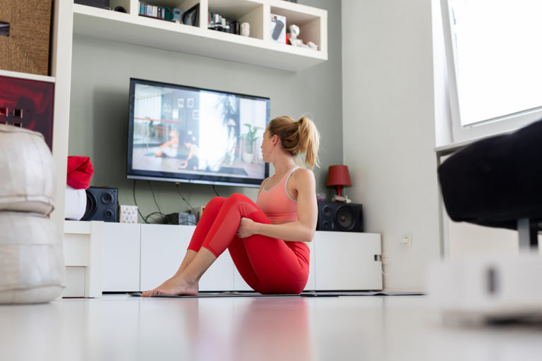 Attractive sporty woman working out at home, doing pilates exercise in front of television in her living room. Social distancing. Stay healthy and stay at home during corona virus pandemic