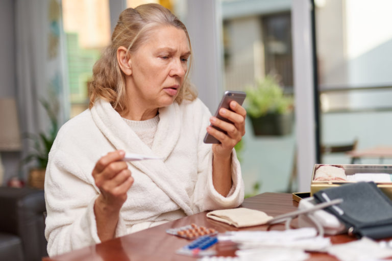 Sickness, seasonal virus problem concept. Senior woman being sick having flu at temperature on thermometer.