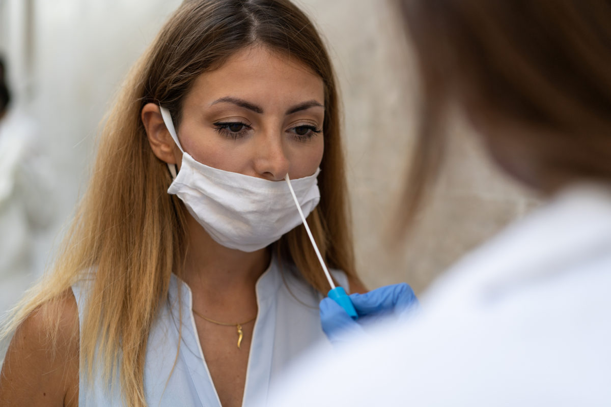 Doctor making a swab test to a young blonde woman for corona virus (covid 19) pandemic disease