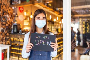 Small business owner with face mask holding the sign for the reopening of the place after the quarantine due to covid 19. Woman with protective mask holding sign we are open, support local business.