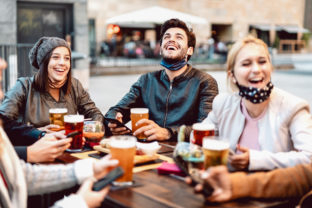 Young friends drinking beer wearing face mask - New normal lifestyle concept with people having fun together talking on happy hour at outside brewery bar - Bright warm filter with focus on central guy