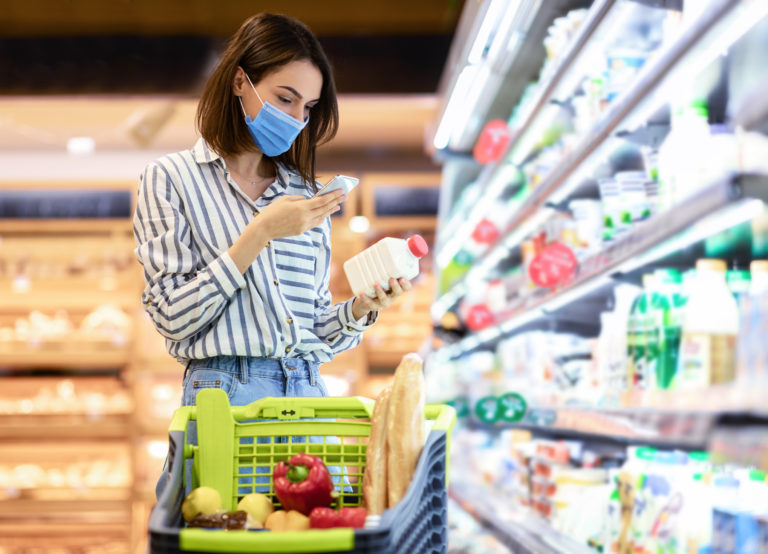 Woman in mask scanning code on products using smartphone