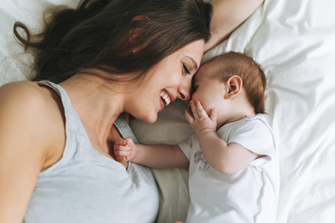 Young mother having fun with cute baby girl on the bed, natural tones, love emotion