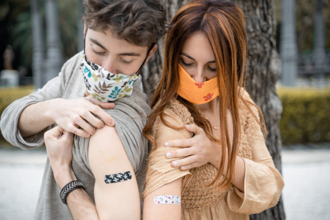 Couple of young people showing the  bandage on the arm after getting the vaccination from coronavirus. New normal concept of people received the vaccine.