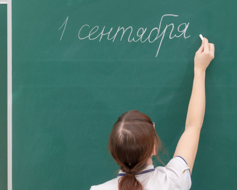 School teacher young woman in a white blouse in the classroom on a blackboard writes with chalk. translation - September 1. portrait