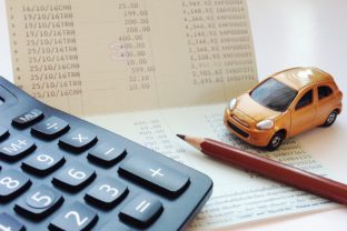 Miniature car model, calculator and saving account book or financial statement on office desk table