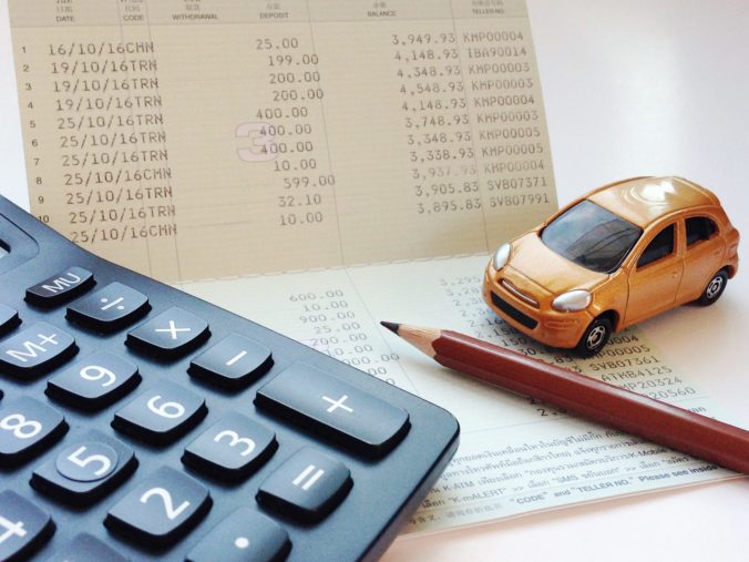Miniature car model, calculator and saving account book or financial statement on office desk table