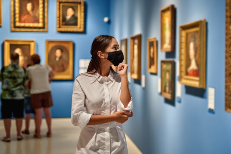 Woman visitor wearing an antivirus mask in the historical museum looking at pictures.