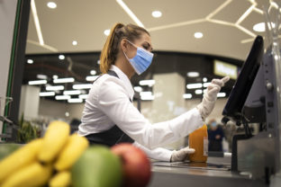 Cashier with protective hygienic mask and gloves working in supermarket and fighting against COVID 19 or corona virus pandemic.