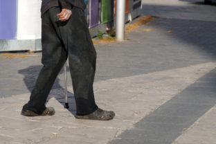 An elderly poor man walks with a cane down the street in dirty clothes, bottom view