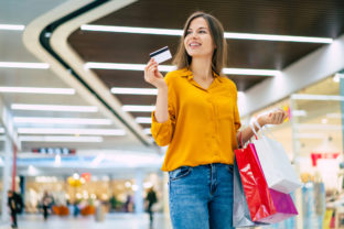 Excited gorgeous smiling young woman is posing with a credit card and shopping bags in the mall