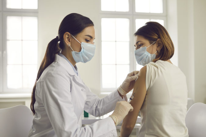 Young woman in face mask getting an antiviral vaccine at the hospital or health center