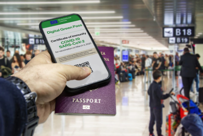 Male hand holding a phone with the European Union vaccination certificate on the screen and a traditional passport inside an airport