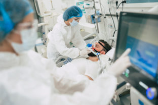 Coronavirus covid 19 infected patient in a quarantine ward at the hospital with doctors in protective suits while they making disease treatment of him