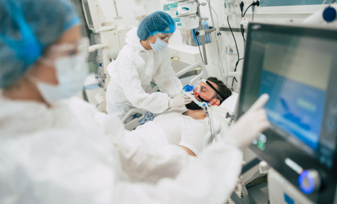 Coronavirus covid 19 infected patient in a quarantine ward at the hospital with doctors in protective suits while they making disease treatment of him