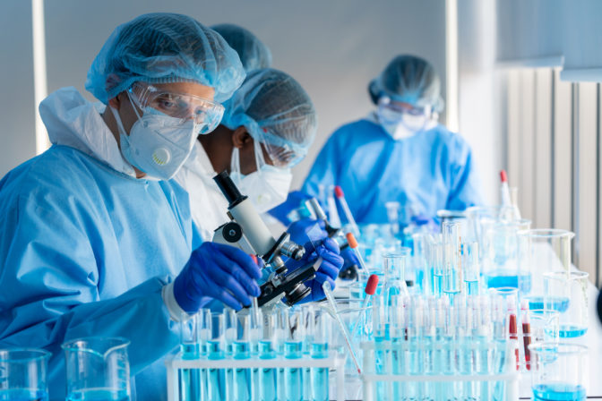 Caucasian Scientists use microscopes to research the covid 19 virus vaccine in a medical laboratory
