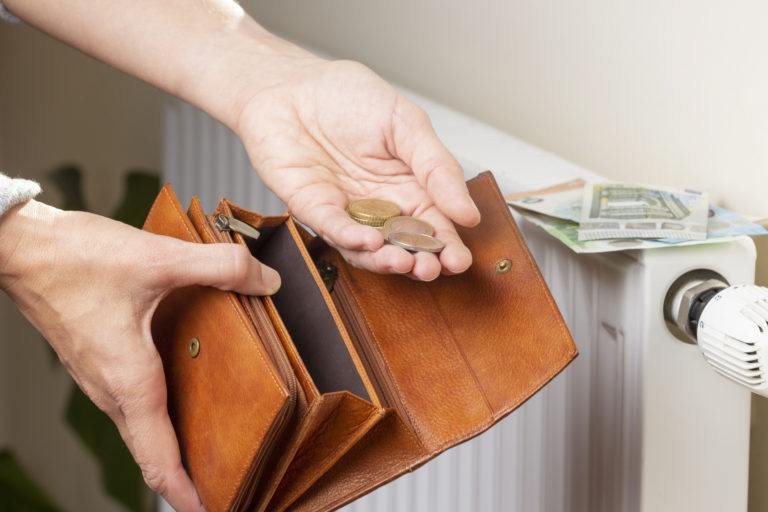 Woman's hand takes euro money from wallet and places on heating radiator battery with temperature regulator. Expensive heating costs during cold season. Paying bills