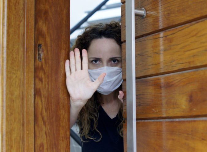 Young female in a medical protection mask looking out the door