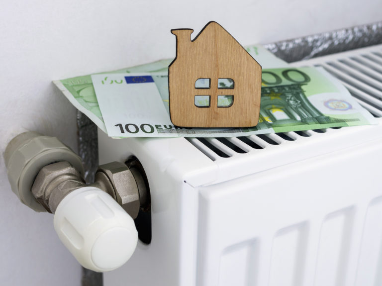 A small wooden house on the background of euro banknotes and radiator heating. Payment for heating in winter. Symbolic image, selective focus.