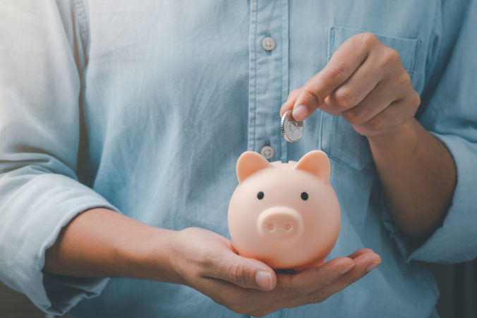 Female hands puts a coin in a pink piggy bank. The concept of saving money.