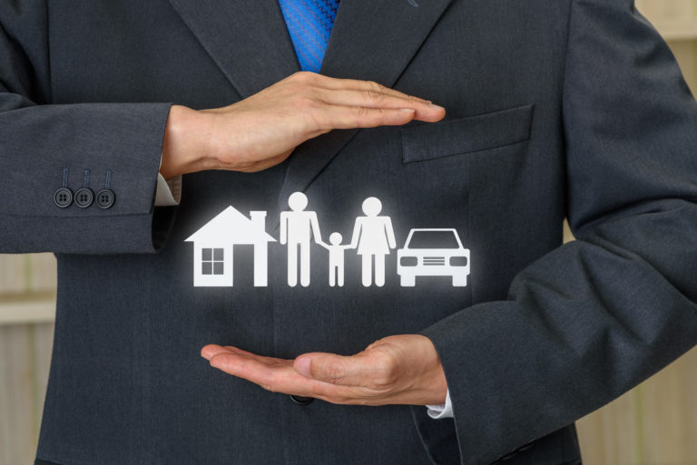 Broker or insurer uses both hands to protect parents e.g. father, mother, child, a house and sedan car