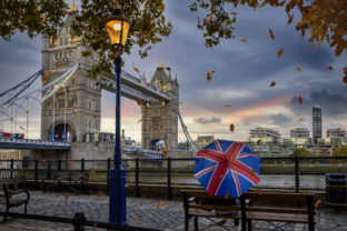 London in autumn time concept with a person holding a british umbrella sitting in front of Tower Bridge
