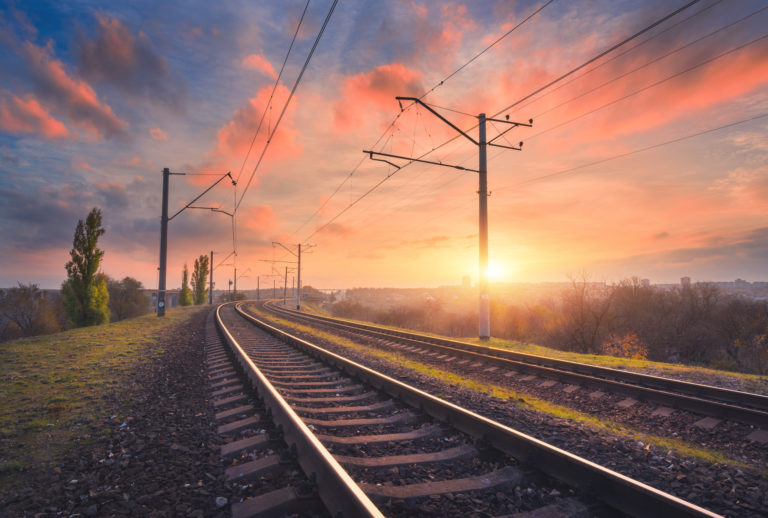 Railroad and beautiful sky at sunset. Industrial landscape with railway station, colorful blue sky with red clouds, trees and green grass, yellow sunlight in summer. Railway junction. Heavy industry
