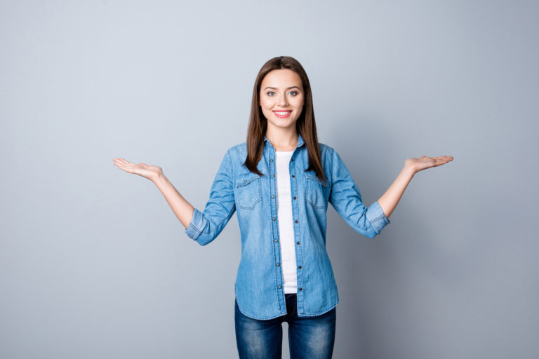 Portrait of successful cheerful cute young woman presenting something, showing copy space on her palm in two sides, looking at camera, standing over grey background