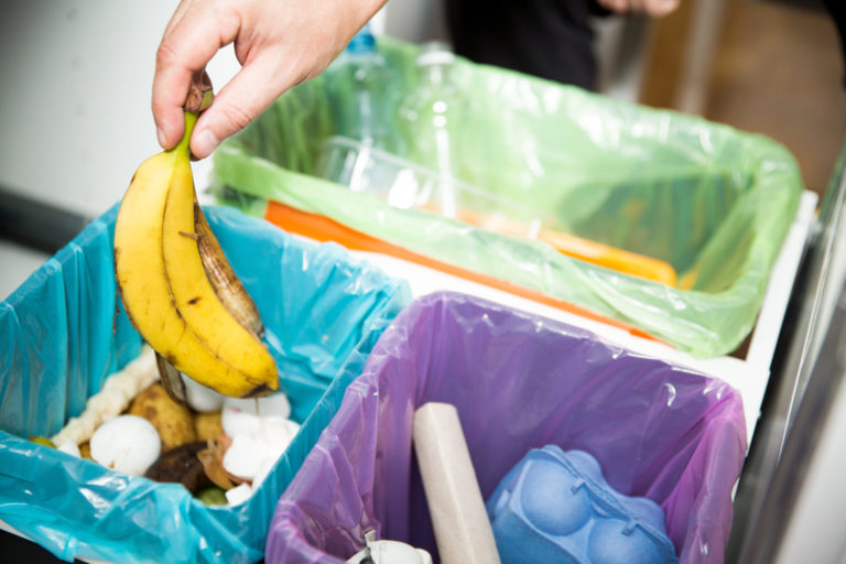 Woman putting banana peel in recycling bio bin in the kitchen. P