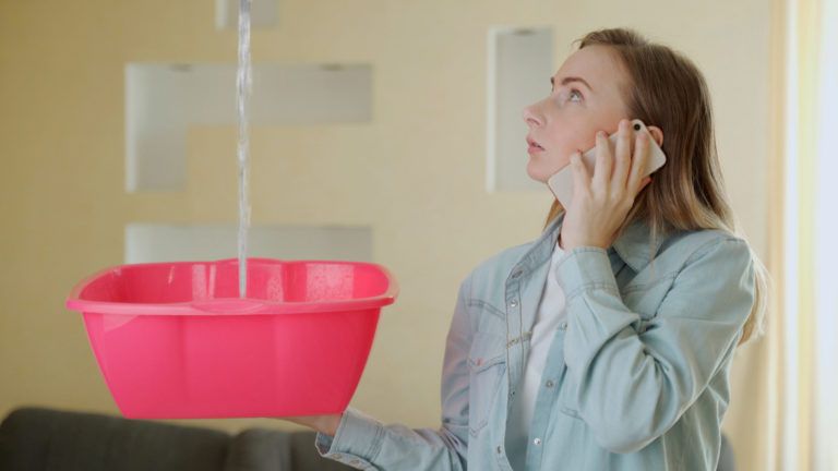 Upset household calling roof repair service while water leaking from ceiling